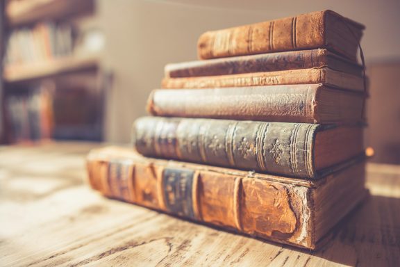 A stack of antique books on a wooden table.